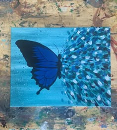 a blue butterfly is on a piece of paper with paint splatters all over it