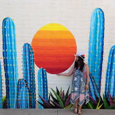 a woman is standing in front of a wall painted with cactuses and the sun