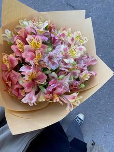 a bouquet of pink and yellow flowers sitting on top of a person's hand