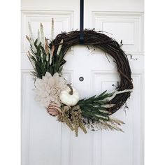 a wreath hanging on the front door with flowers and foliage around it, in front of a white door