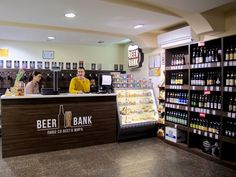 a man standing behind a counter in a store with beer bottles on the shelves and people walking by