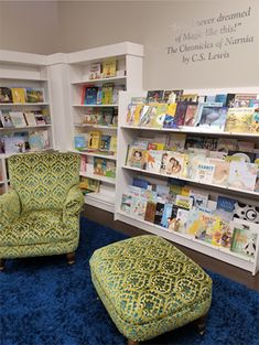 two green chairs and a foot stool in front of a book shelf filled with books