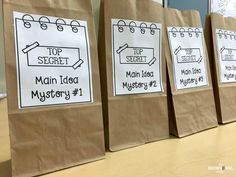 three brown paper bags with signs on them sitting on a wooden table in front of a bulletin board