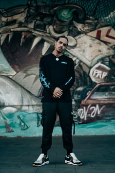 a man standing in front of a graffiti wall wearing black sweatpants and white sneakers