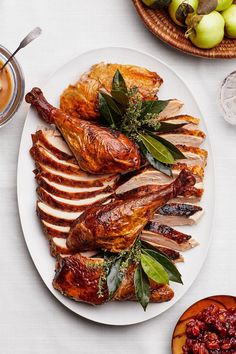 a white plate topped with sliced turkey next to bowls of fruit and sauces on a table