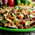 a green plate filled with taco salad on top of a table next to tomatoes