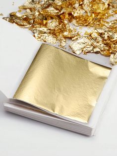 some gold flakes are laying on top of a white box with a piece of paper next to it