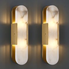 two wall lights mounted to the side of a wall with marble and gold trimmings