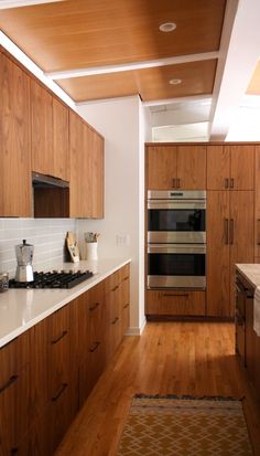 a kitchen with wooden cabinets and white counter tops, along with a rug on the floor