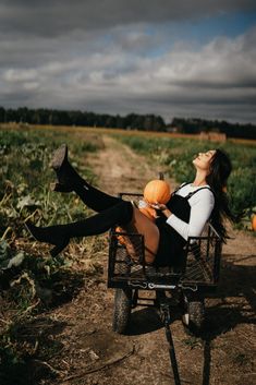 a woman sitting in a wheelbarrow with pumpkins on her lap and looking up into the sky