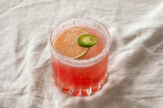 a close up of a drink in a glass on a white cloth with a lime slice