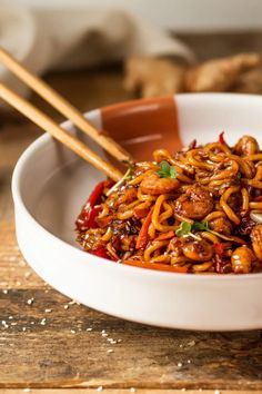 two chopsticks sticking out of a bowl filled with noodles and sauce on a wooden table