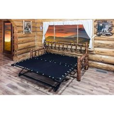 a bed frame in front of a log cabin window with mountains and sky behind it