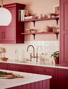 a kitchen with red cabinets and white counter tops, along with shelves filled with dishes