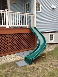 a green slide sitting in front of a house next to a wooden deck and fence