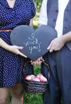 a man and woman holding a heart shaped chalkboard with the words pick you written on it