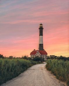 a light house sitting on top of a lush green field next to a dirt road