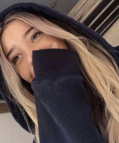 a woman with long blonde hair wearing a black hoodie and looking at the camera