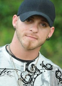 a man wearing a black hat and silver shirt is looking at the camera with a serious look on his face