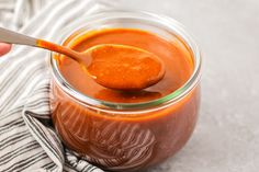 a spoon full of sauce sitting on top of a glass jar next to a towel