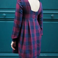 a woman standing in front of a green door wearing a purple and blue plaid dress