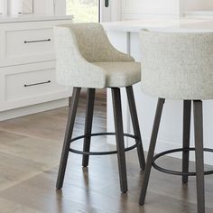 two bar stools sitting in front of a kitchen island with white cabinets and drawers