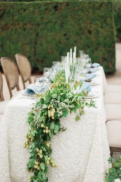 the table is set with white linens and greenery