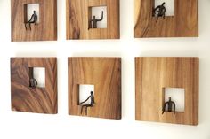 four square wooden plaques mounted to the side of a wall with metal hooks on them