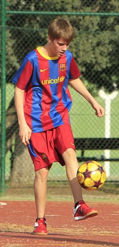 two young men playing soccer on a field with one kicking the ball while the other dribbles it