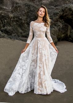 a woman standing on top of a sandy beach wearing a white dress and long sleeves