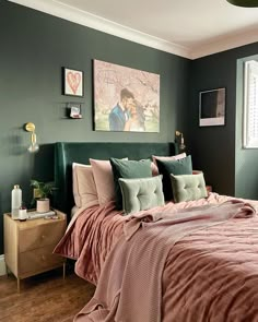 a bed with pink and green comforter in a bedroom next to a painting on the wall