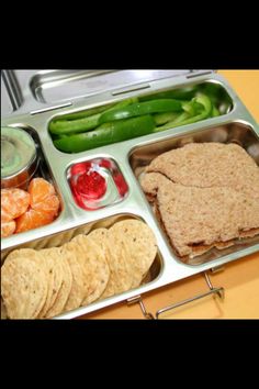 a metal lunch box filled with food and veggies on top of a table