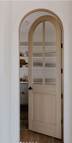 an arched wooden door with glass panels in a white walled entryway to a kitchen