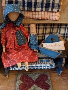 two dolls are sitting on a bench in front of some pillows and rugs with the word america written on them