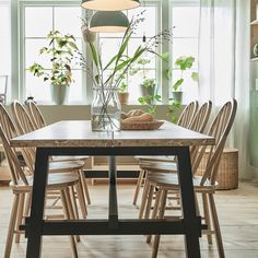 a wooden table with chairs around it in front of a window filled with potted plants