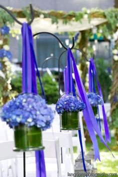 two vases filled with blue flowers and purple ribbon tied to the back of them