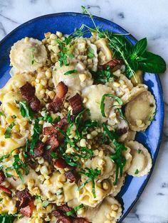 a blue plate topped with macaroni and cheese covered in meat, herbs and sauce