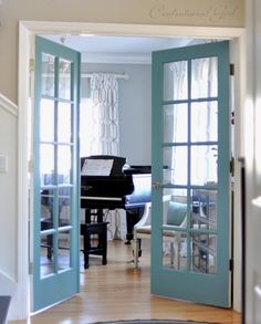 an open door leading into a living room with piano in the corner and blue doors