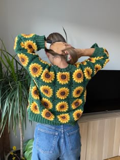 a woman standing in front of a tv wearing a green sweater with sunflowers on it