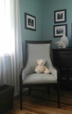 a white teddy bear sitting in a chair next to a dresser and pictures on the wall