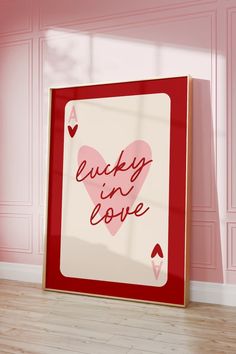 a red and white frame with the words lucky in love on it next to a pink wall