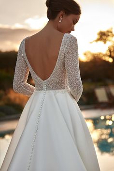 a woman in a wedding dress standing next to a swimming pool with her back turned towards the camera