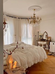 a bedroom with white bedding and chandelier hanging from the ceiling next to two candles