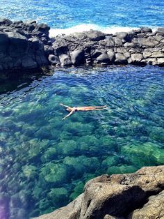 a person swimming in the water near some rocks and blue water with green algae growing on it