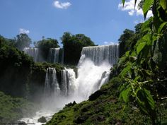 the waterfall is surrounded by greenery and blue skies in the background, with water cascading over it