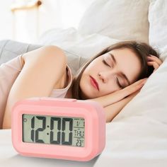 a woman laying in bed next to a pink alarm clock with thermometer on it