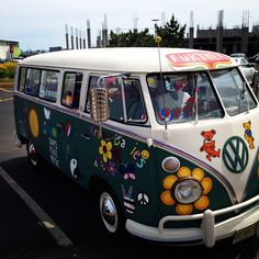 an old vw bus is decorated with stickers and flowers on the front, parked in a parking lot