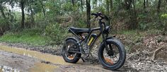 a black bike parked on the side of a muddy road in front of some trees