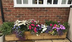 a wooden planter filled with lots of flowers next to a brick wall and door