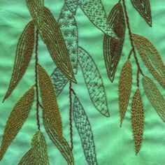 a close up view of some leaves on a green cloth with gold threadwork and sequins